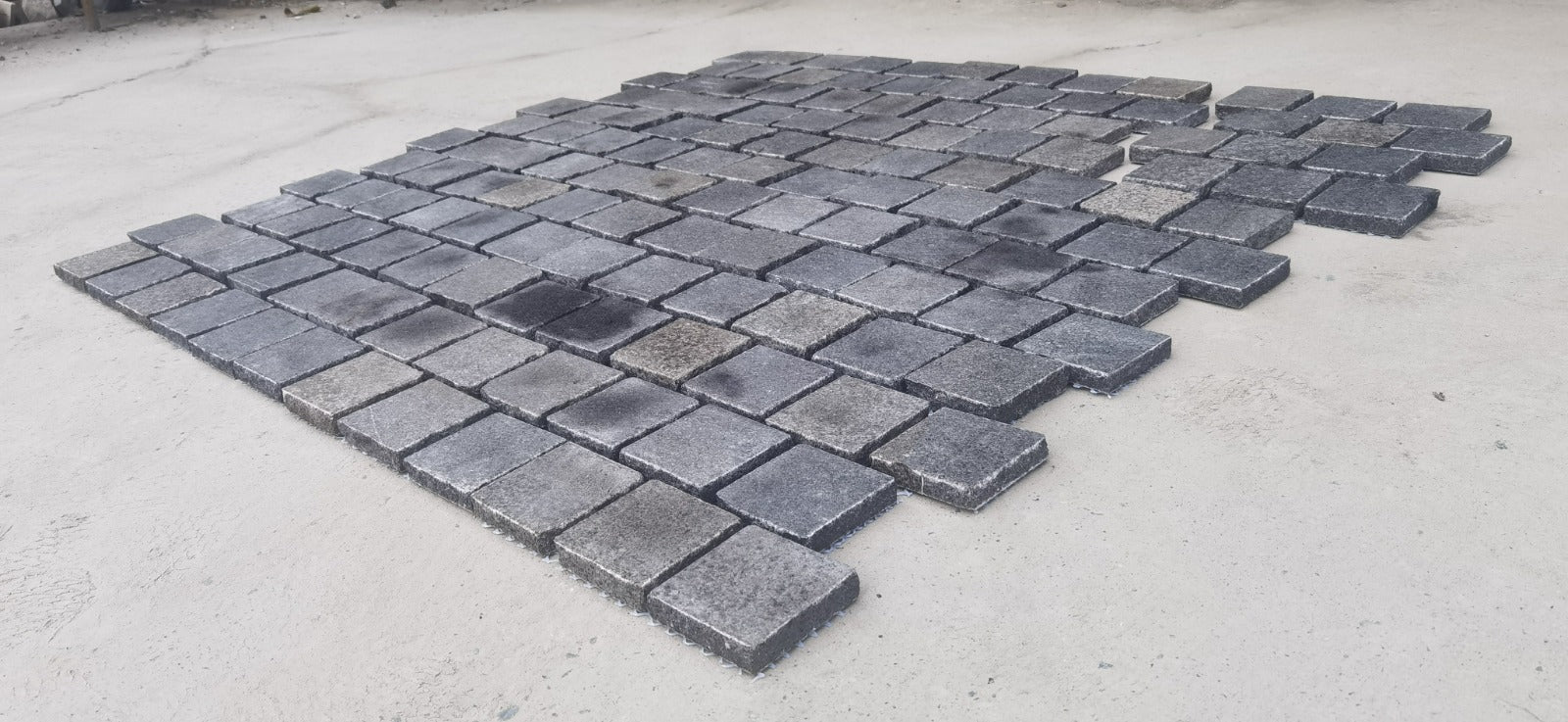 Black granite cobble stone from The Nurso, showing textured surface and irregular shape for durable outdoor paving.