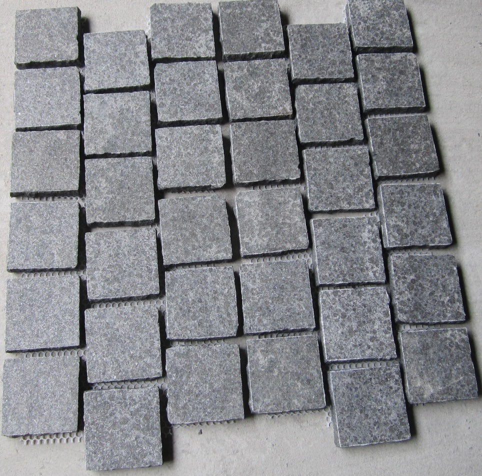 Black granite cobblestone from The Nurso featuring rough textured surface and irregular shape for outdoor paving.